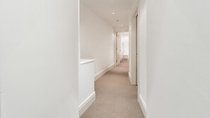 A narrow hallway with white walls and a patterned carpet. - PML Apartments Park Road (London)