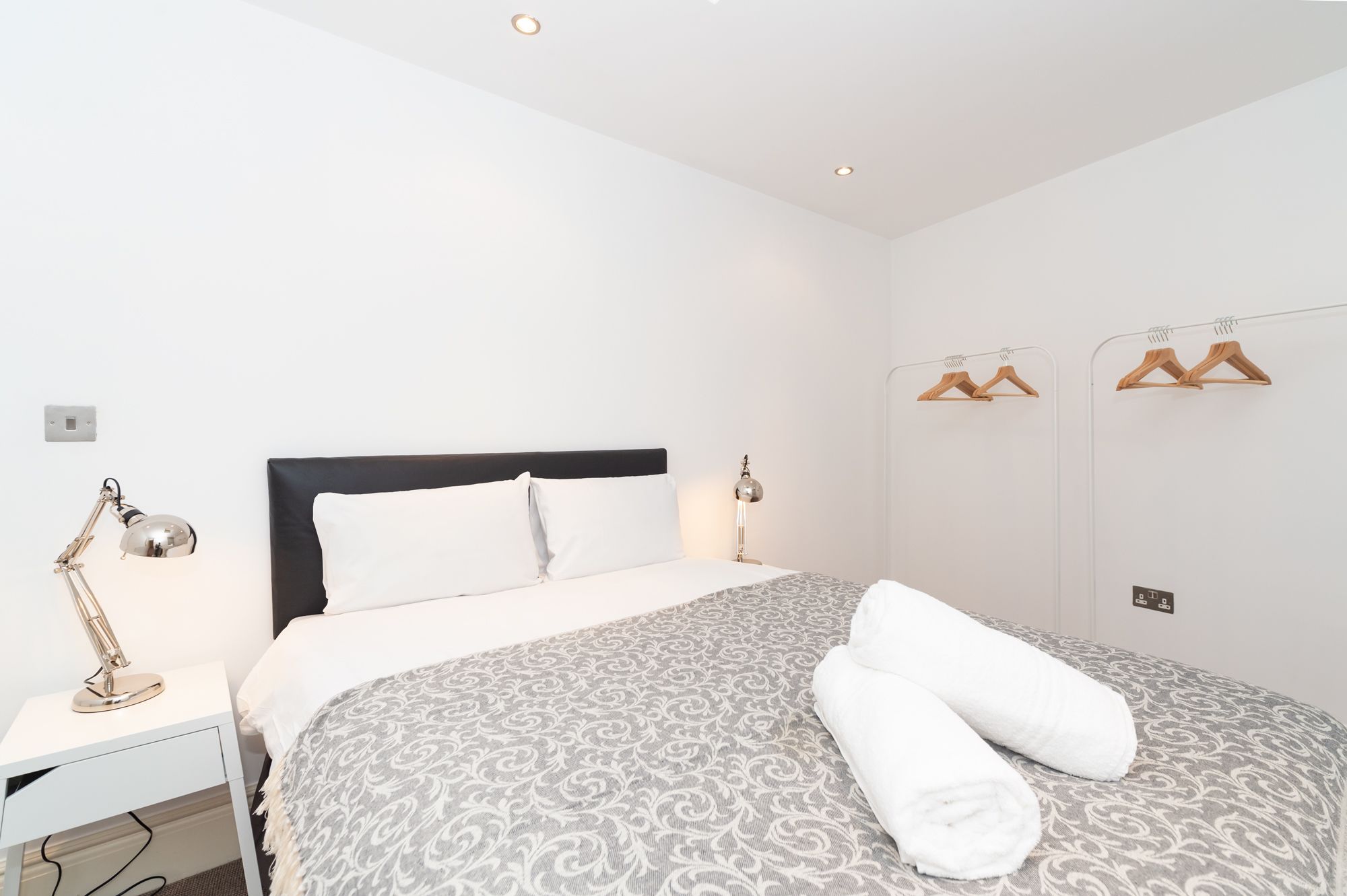 A neatly arranged bedroom with a bed, bedside lamps, a wardrobe, and a mirror.