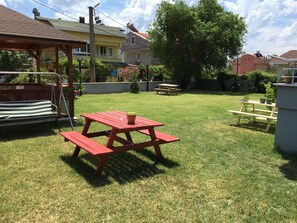 Un jardin avec une table de pique-nique rouge, une balançoire et un petit espace aménagé en jardin.