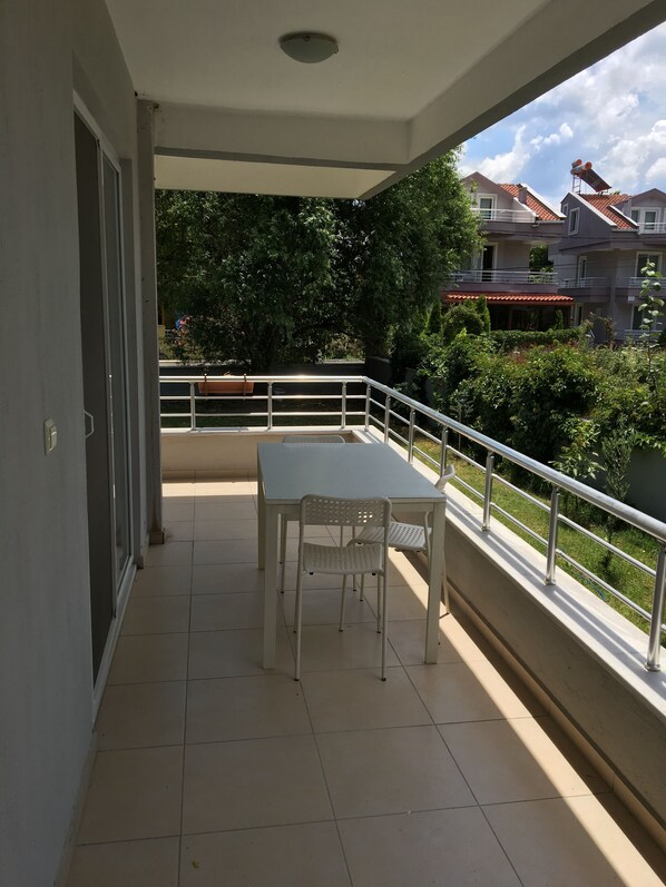A balcony with a table and chairs, a railing, and a view of surrounding buildings and greenery. - Cam Apart Hotel (Erdek)