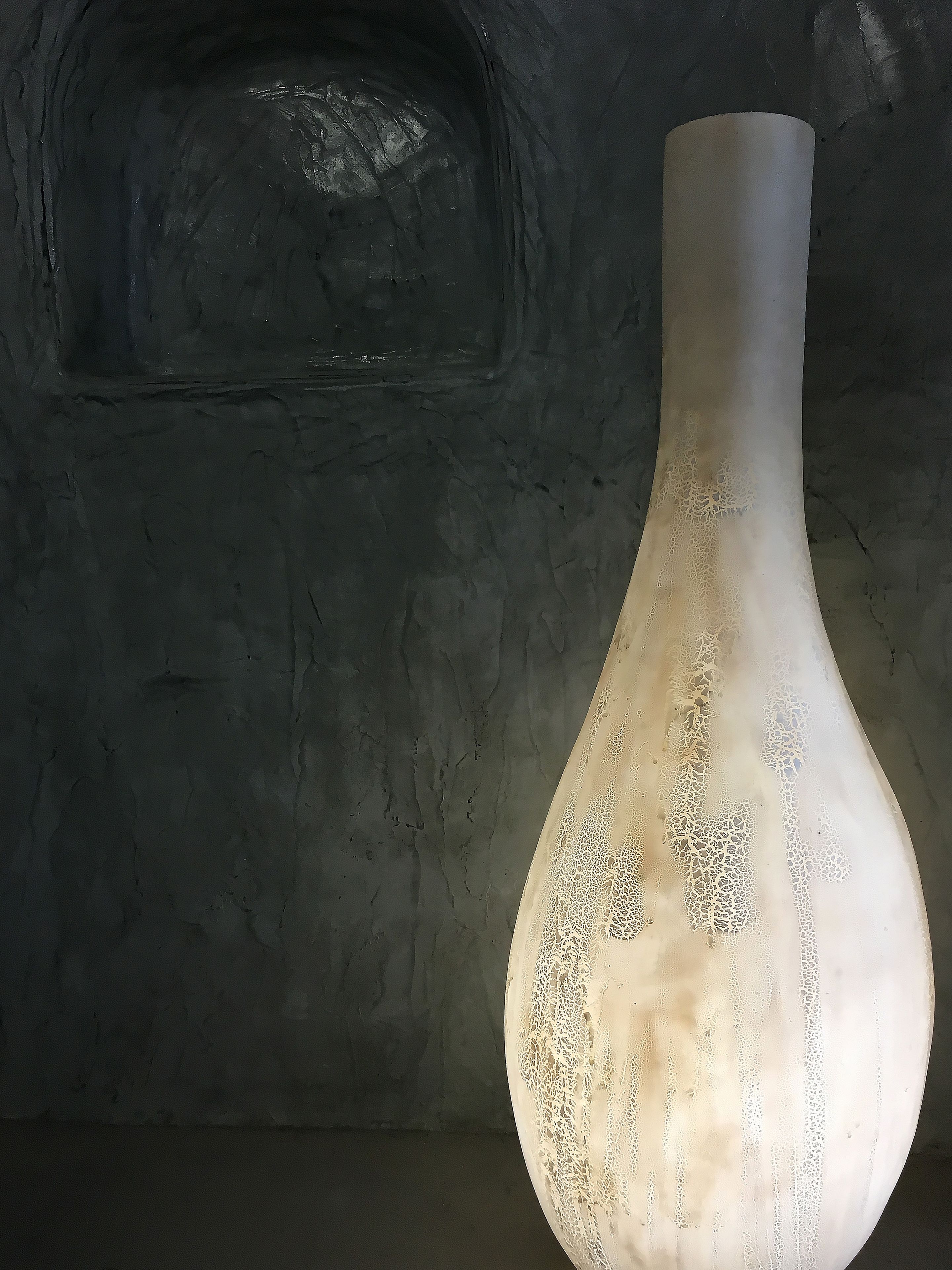 Un jarrón blanco con diseños intrincados sobre un muro con textura.