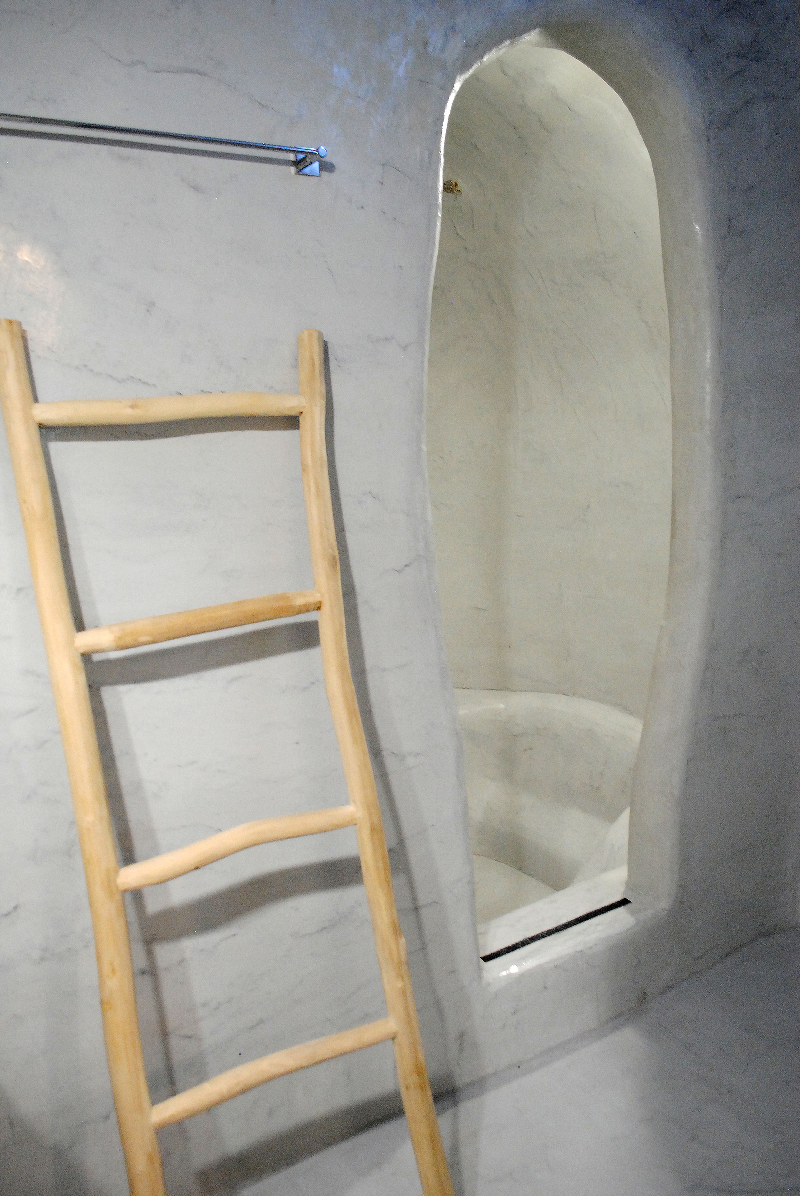 A room with a wooden ladder leaning against a wall, an arched window, and a marble floor.