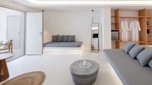 Een moderne woonkamer met een grijze bank, een rond ottoman, een grijze bankje en een houten garderobe met gewaden.