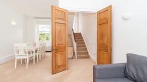 Una habitación con sofá gris, escalera de madera y comedor con sillas blancas y una mesa.