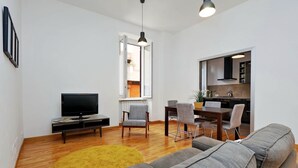 Een moderne woonkamer met een flatscreen televisie, een grijze bank en een geel vloerkleed.