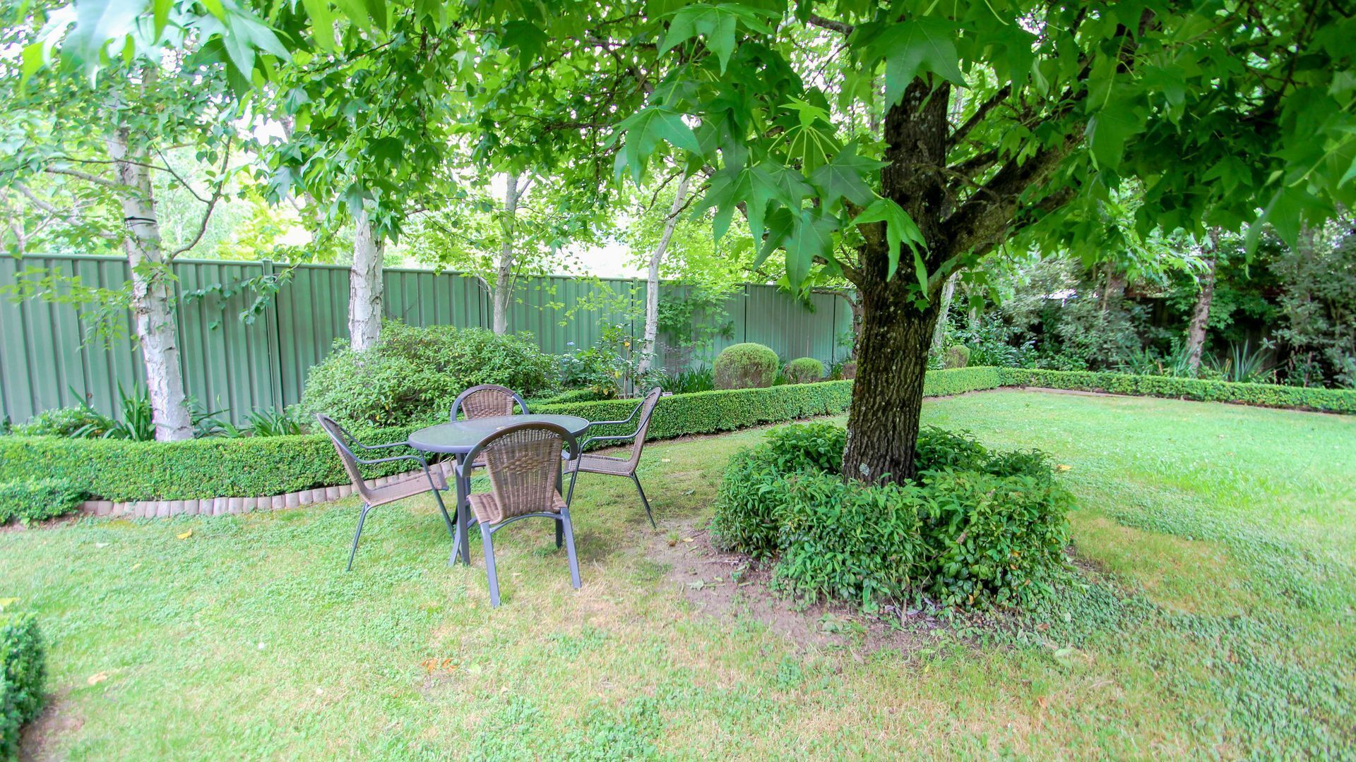 Un jardin avec une table et des chaises pour les repas, entouré d’une pelouse et de haies bien entretenues.