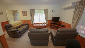 Een woonkamer met een bank, twee fauteuils, een salontafel, een televisie en een airconditioner.
