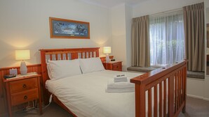 Een hotelkamer met een houten bed, twee nachtkastjes met lampen, een schilderij aan de wand en een raam met gordijnen.