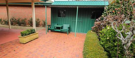 A patio area with a brick floor, a green bench, and a covered seating area with a green roof.
