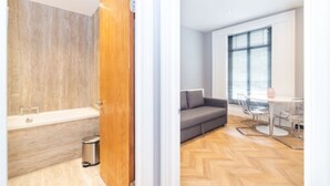 A modern bathroom with a bathtub and a wooden door, and a living area with a sofa, table, and chairs.
