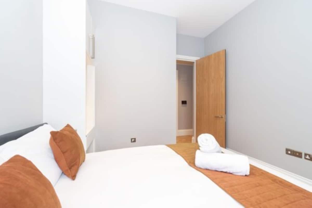 A modern hotel room with a large bed, a wooden door, and a view of the hallway.