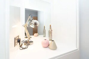 A white desk with a desk lamp, a pink vase, and two bottles.