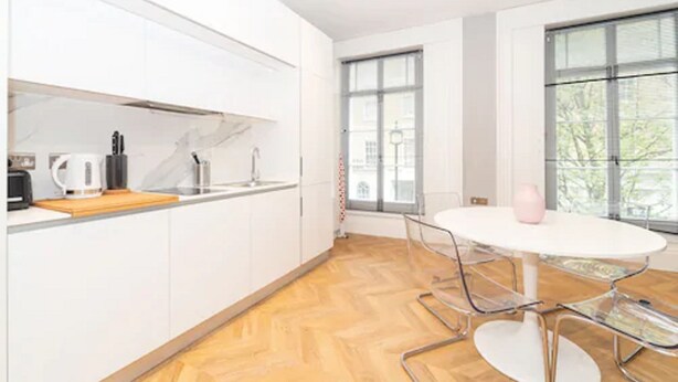 A modern kitchen with white cabinets, a wooden countertop, and a white dining table with metal chairs.