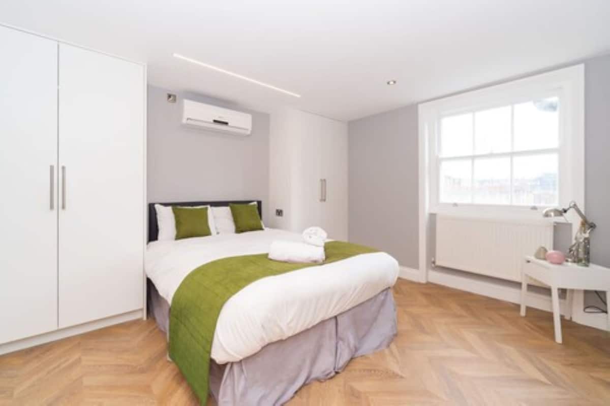 A bedroom with a bed, white wardrobe, radiator, and a window with a view.