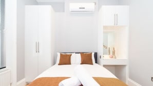 A hotel room with a bed, white wardrobe, and a wall-mounted air conditioner.