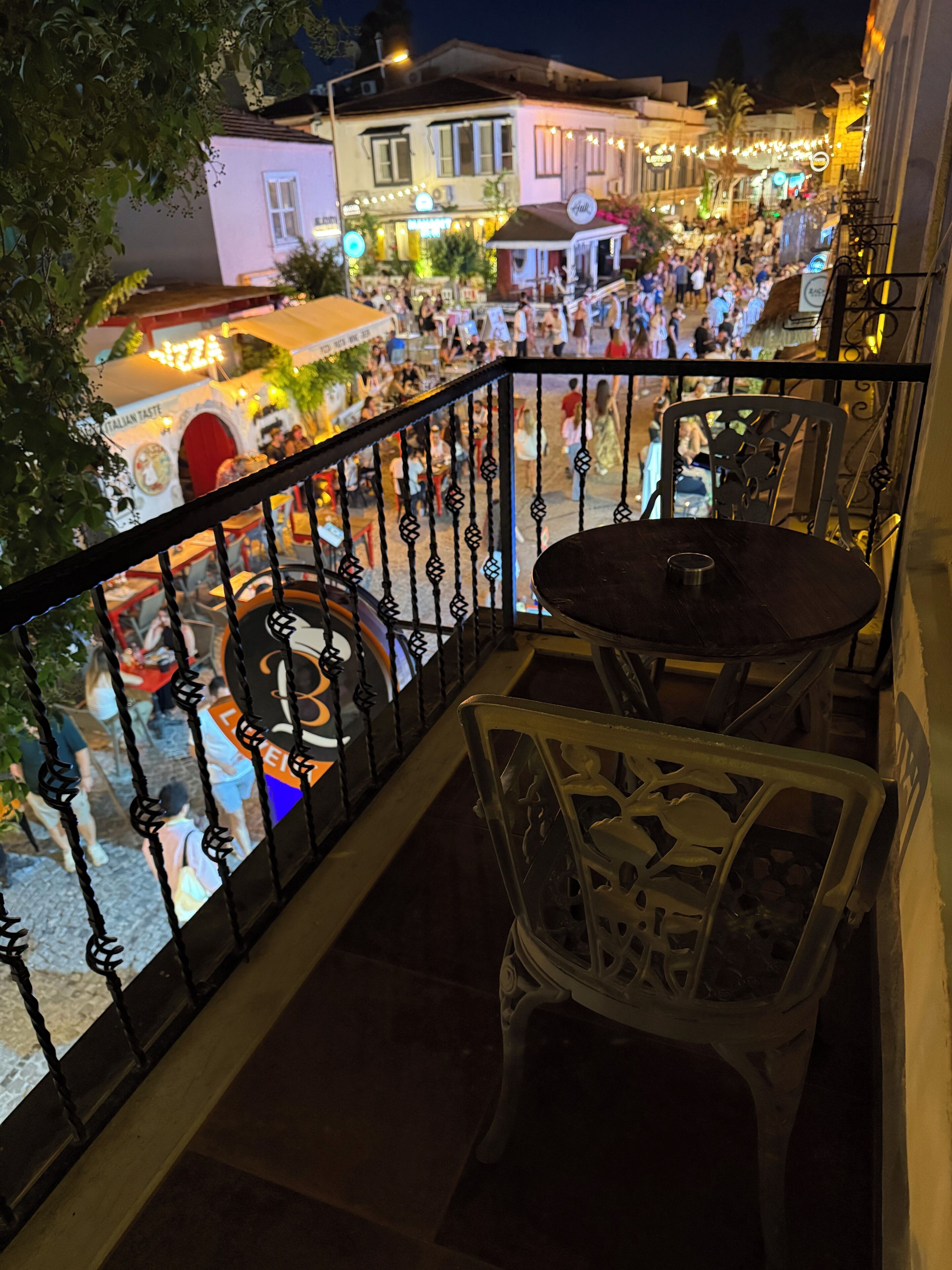 A balcony with a table and chairs, overlooking a busy street with shops and people.