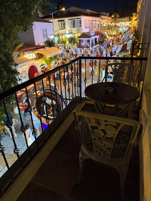 Ein Balkon mit Tisch und Stühlen, der auf eine belebte Straße mit Geschäften und Menschen blickt.