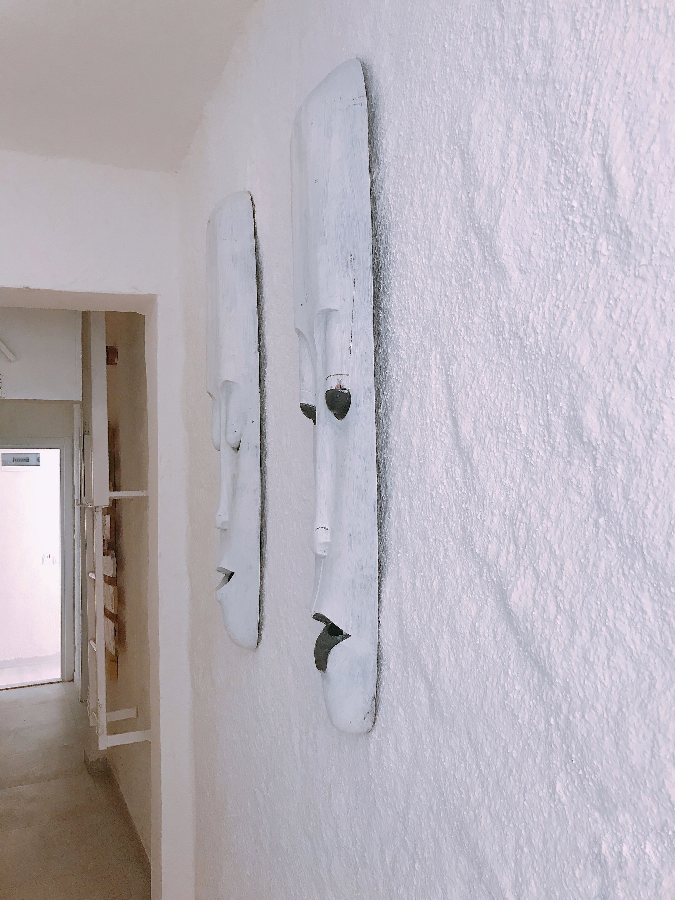 A hallway with white walls and two white, textured wall decorations.