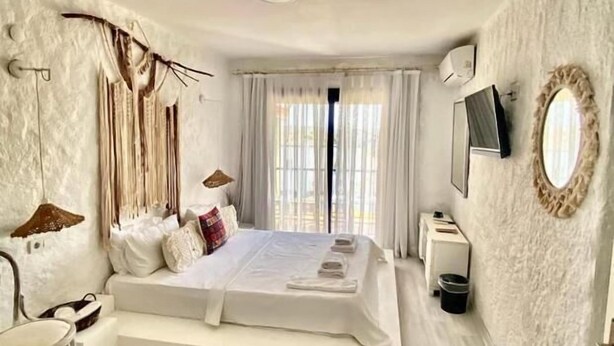 Un dormitorio moderno con una cama grande, una mesita de noche, una silla, un televisor y un espejo en la pared.