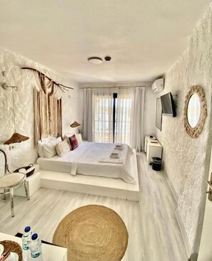 Une chambre moderne avec un grand lit, une table de chevet, une chaise, un téléviseur et un miroir au mur.