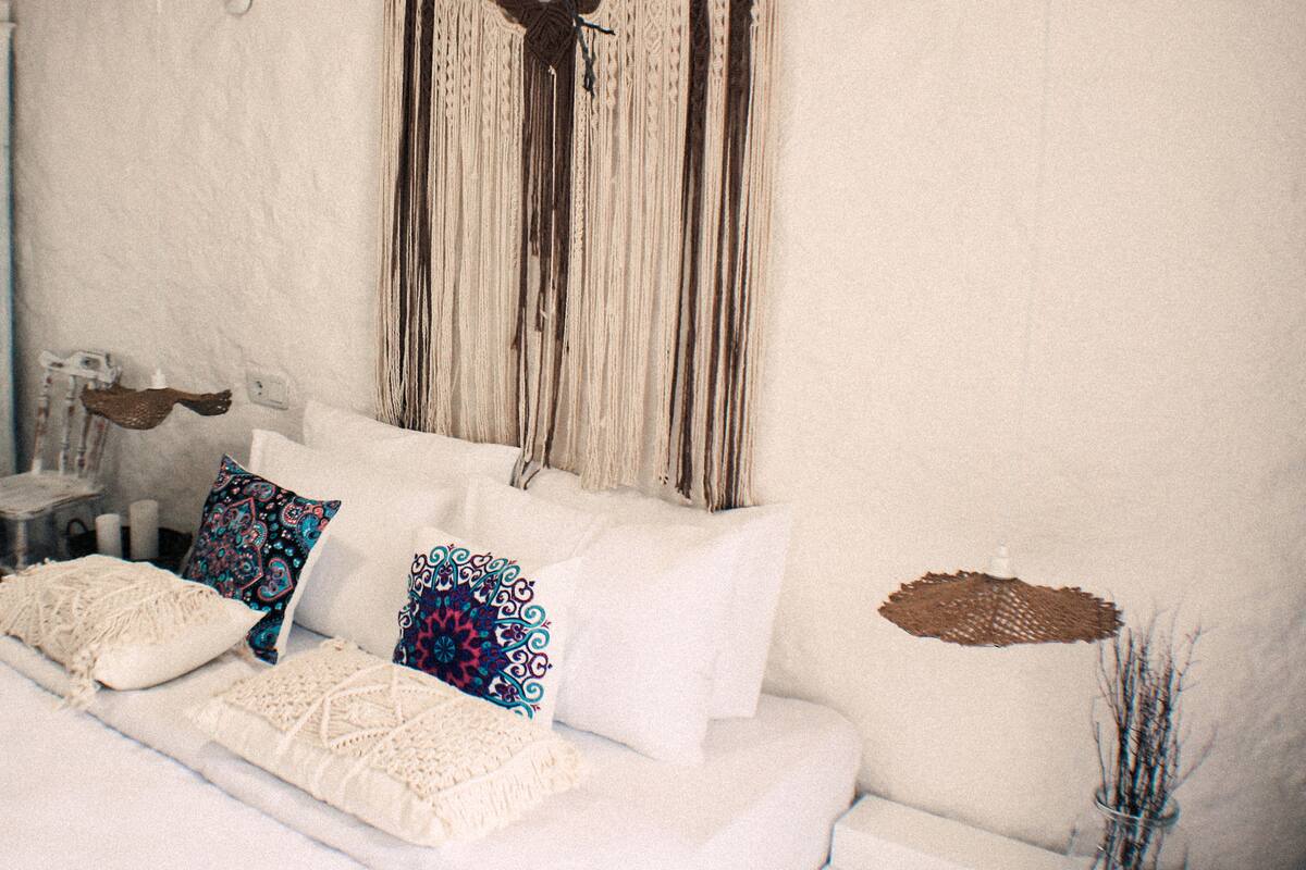 A white sofa with patterned cushions, a macrame wall hanging, and a vase with branches.