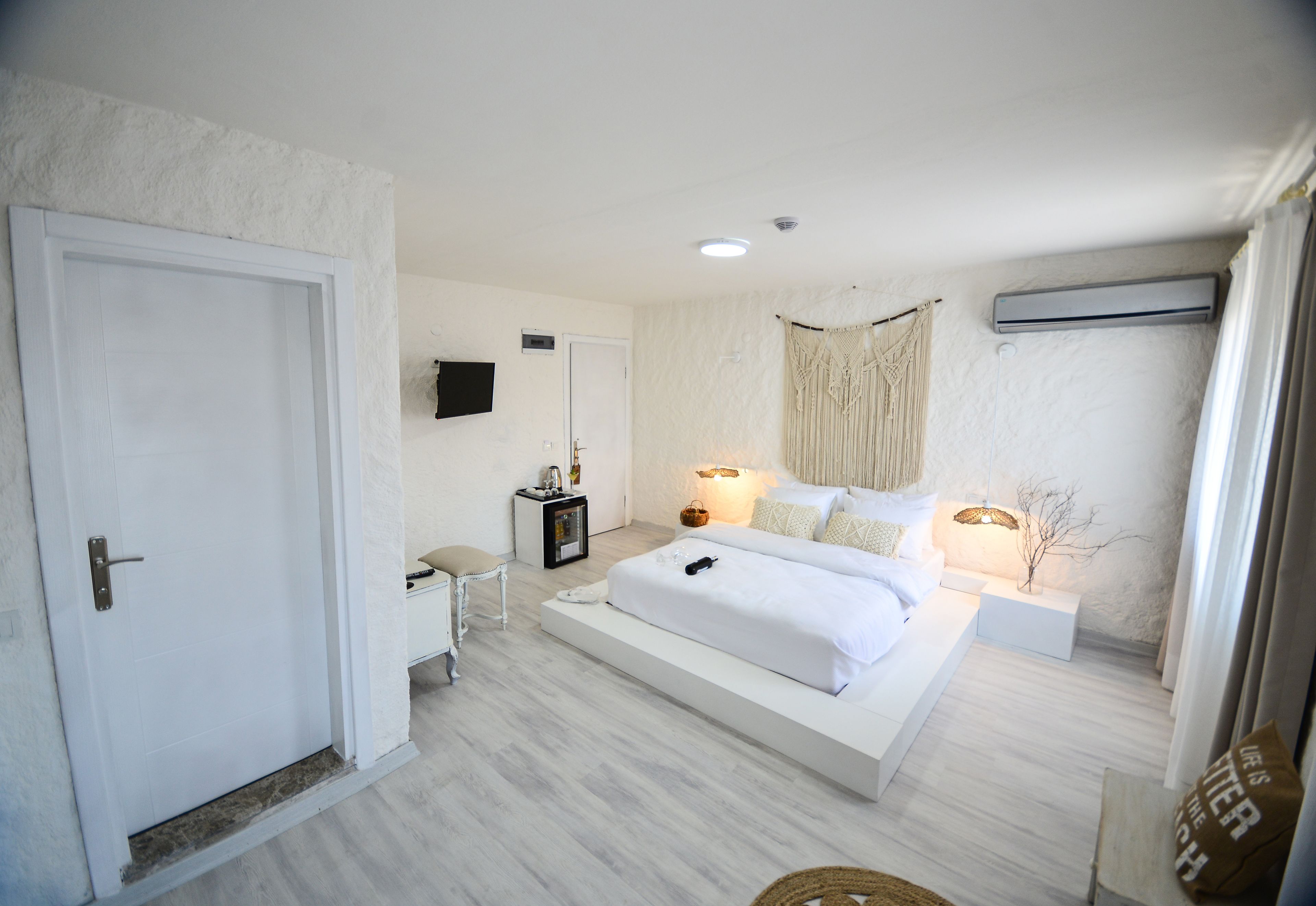 A modern bedroom with a large bed, bedside tables, a TV, and a wall-mounted air conditioner.