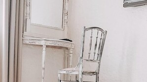 Una habitación con un espejo de marco blanco, una mesita pequeña y una silla de plástico transparente.