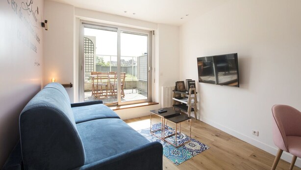 Un soggiorno moderno con un divano, una televisione e un balcone con tavolo e sedie.