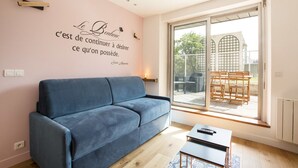 Un soggiorno moderno con un divano blu, un tavolino e un'ampia porta scorrevole in vetro che dà su un patio esterno con mobili in legno.