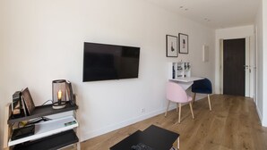 Un soggiorno moderno con una TV a schermo piatto montata a parete, una piccola scrivania con una sedia e una libreria.