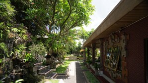Un sentier bordé de plantes en pot et agrémenté d’une petite cascade, qui mène à un bâtiment aux éléments architecturaux traditionnels.