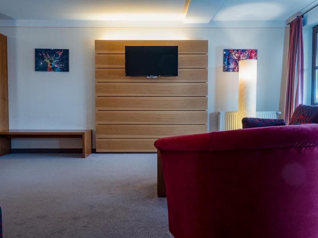 A modern living room with a flat-screen TV mounted on a wooden panel wall, a red sofa, and a bench.