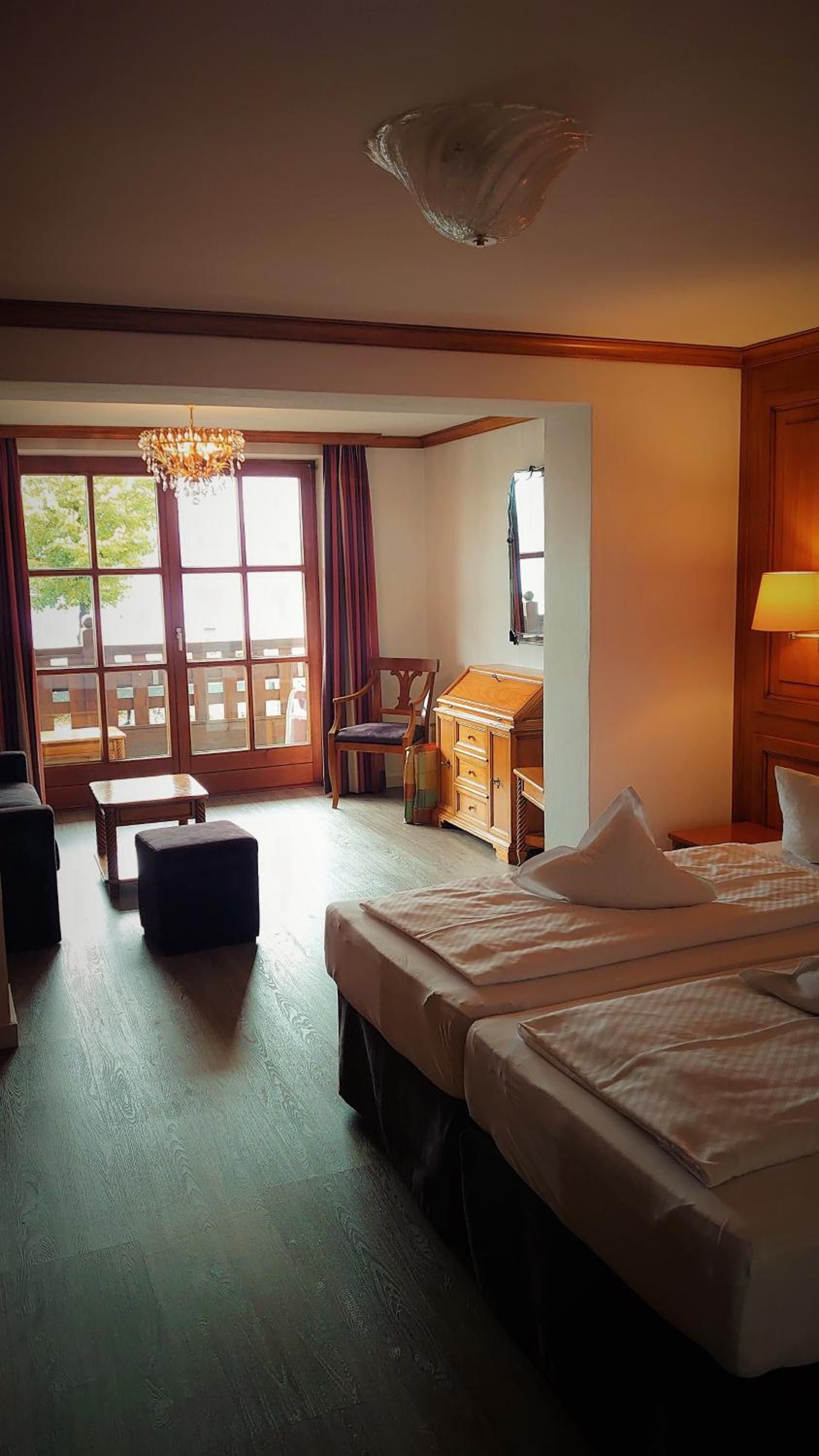 A hotel room with a large window, a desk, two beds, a chair, and a small table.