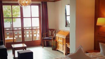 A hotel room with a large window, a desk, two beds, a chair, and a small table.