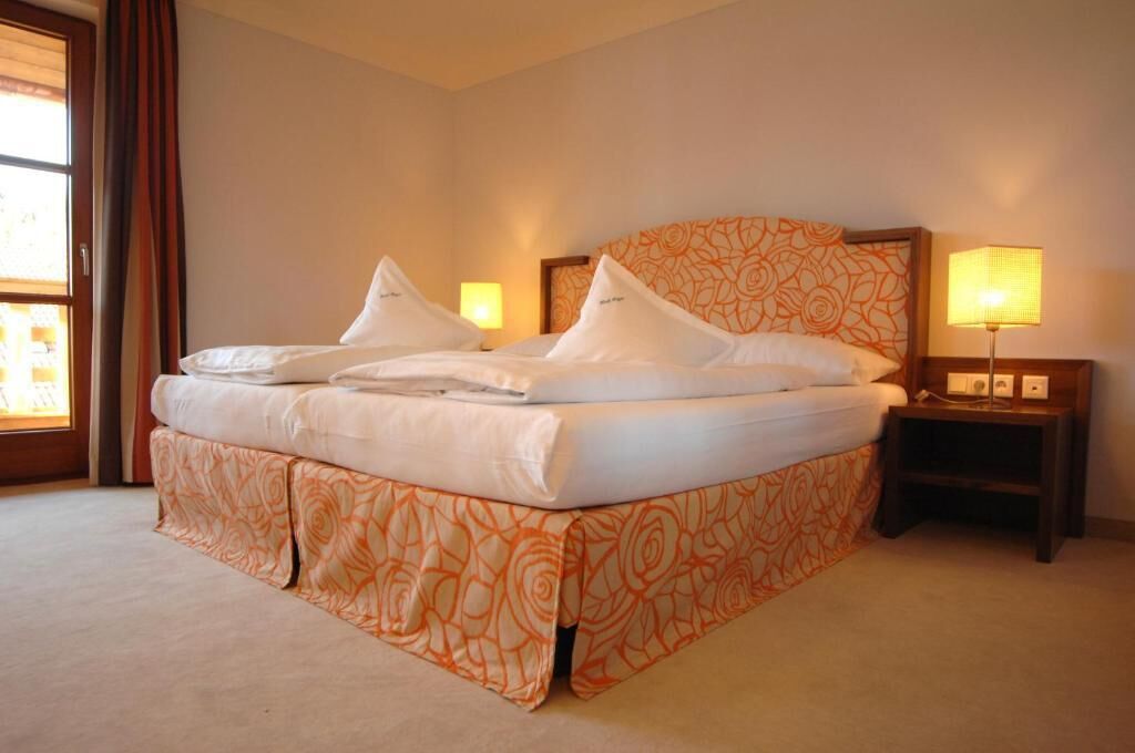 A hotel room with a large bed, two bedside lamps, and a window with curtains.