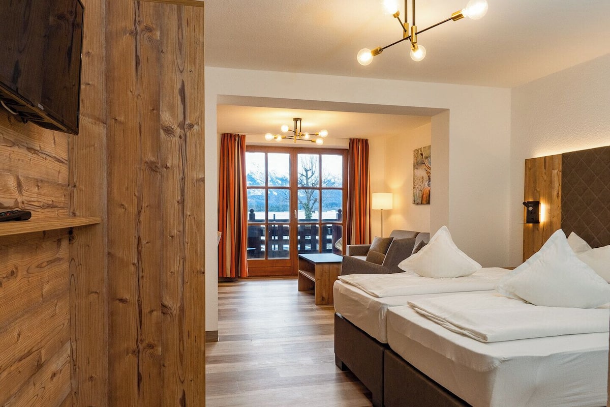 A hotel room with a wooden wall, a bed, a sofa, a desk, and a balcony with a view.
