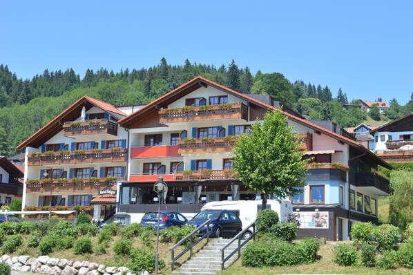 A multi-story hotel with balconies, a parking area, and a mountainous backdrop.
