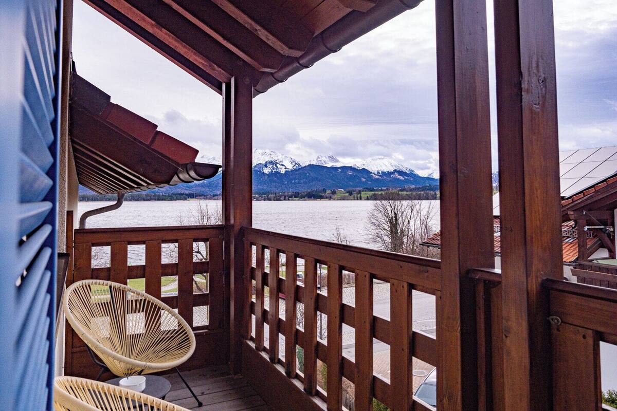 A wooden balcony with a view of a lake and mountains.