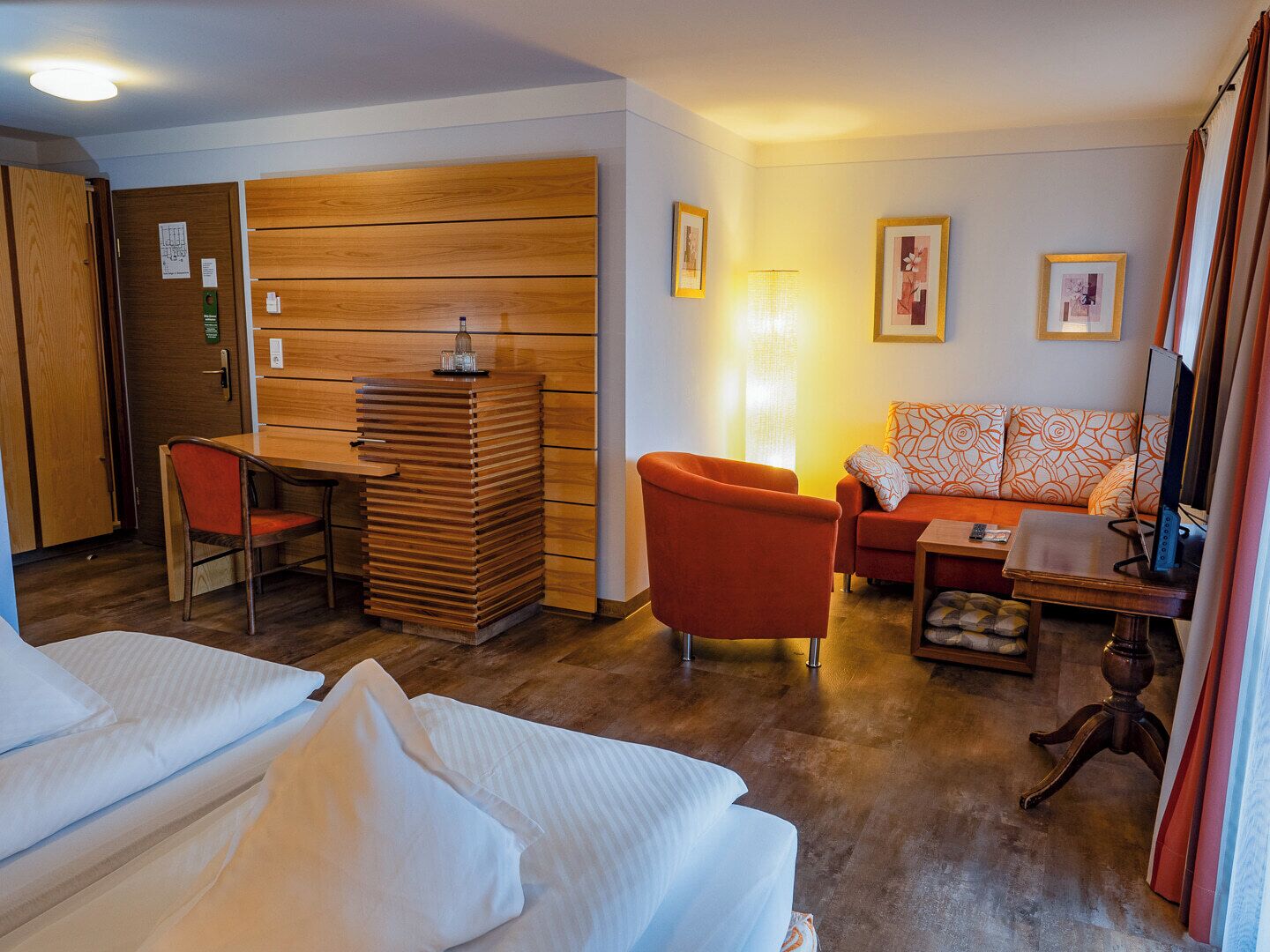 A hotel room with a wooden desk, a sofa, a TV, and two beds.