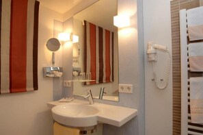 A hotel bathroom with a sink, mirror, and towel rack.