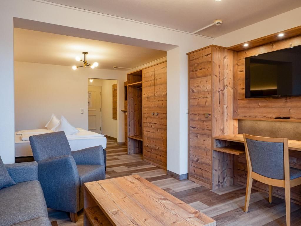 A modern room with a wooden floor, a bed, a desk, and a TV mounted on the wall.