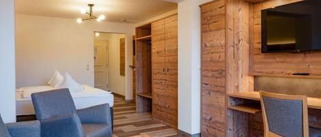 A modern room with a wooden floor, a bed, a desk, and a TV mounted on the wall.