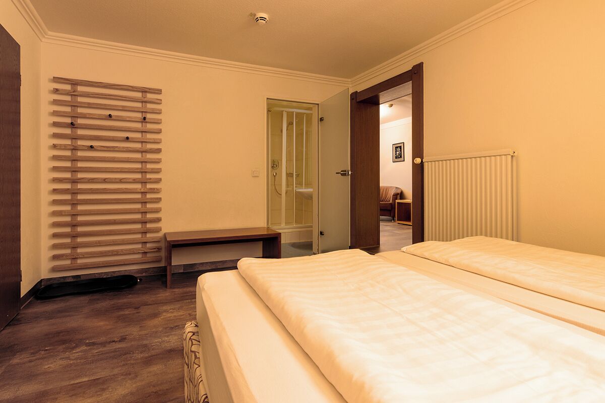 A hotel room with a bed, a bench, a radiator, and a wooden slat wall.