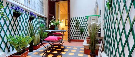 A small courtyard with a table and chairs, surrounded by potted plants and a lattice fence.