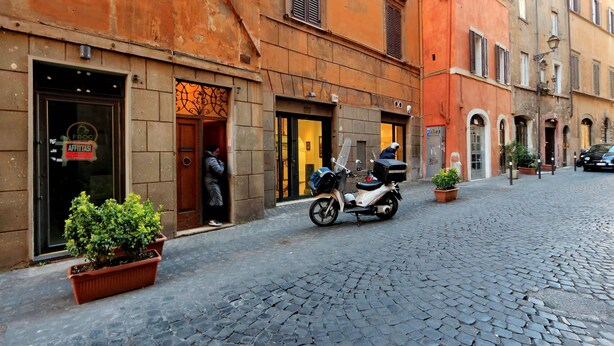 A cobblestone street with a scooter parked in front of a building with a sign that reads "Frog". - Farnese Charme - My Extra Home (Rome)