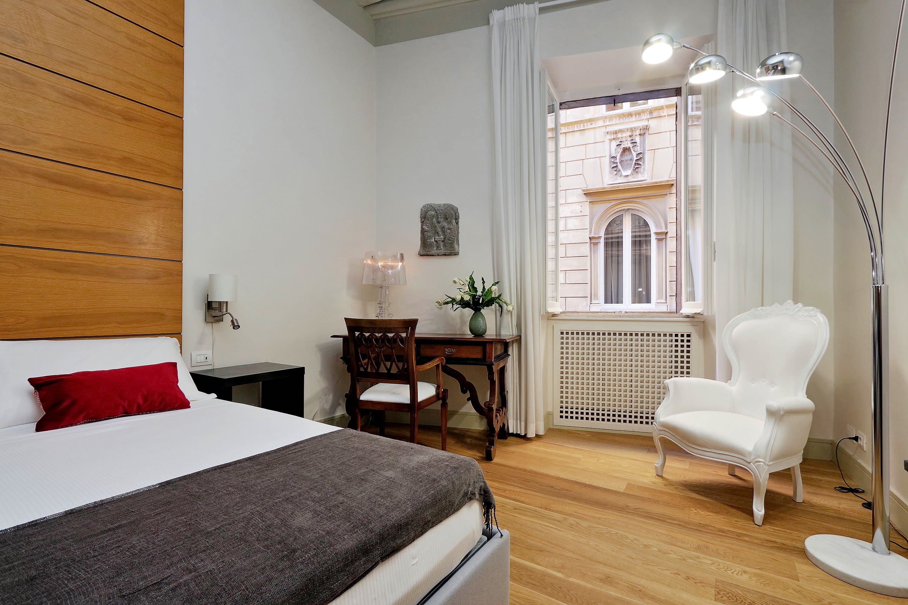 A neatly arranged bedroom with a bed, a desk, a chair, and a floor lamp.