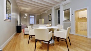 A modern dining area with a round table and six chairs, a white ceiling with wooden beams, and a view of the sea through a large window. - Farnese Charme - My Extra Home (Rome)