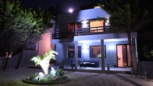 Una casa moderna de dos pisos con balcón, zona de estar al aire libre y un jardín bien iluminado.