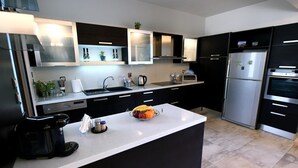 Una cocina moderna con armarios negros, electrodomésticos de acero inoxidable y encimera blanca.