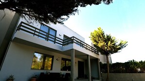 Un edificio moderno de dos pisos con balcón, ventanas amplias y plantas en macetas.